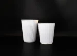 "Two white ribbed coffee cups on a black background, illustrating the sleek packaging design from www.jcpackagingdubai.com."