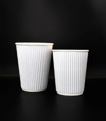 "Two white ribbed coffee cups on a black background, illustrating the sleek packaging design from www.jcpackagingdubai.com."