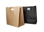 "Two paper bags, one brown and one black, both with cut-out handles, stand next to each other against a light background."