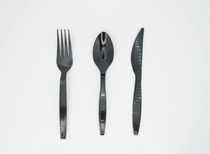 "Sleek black plastic cutlery set including a fork, spoon, and knife on a white background offered by www.jcpackagingdubai.com."