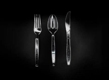 "Elegant clear plastic fork, spoon, and knife on a dramatic black background, available at www.jcpackagingdubai.com."