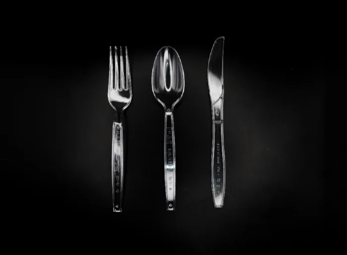 "Elegant clear plastic fork, spoon, and knife on a dramatic black background, available at www.jcpackagingdubai.com."